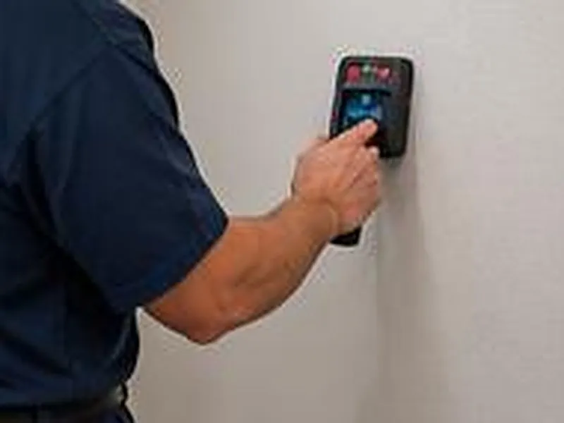 Hand holding a small detector against a wall during an inspection